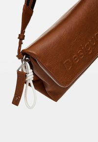 Borsa a spalla in pelle marrone con una finitura testurizzata, caratterizzata da una cerniera argentata, dettagli in metallo bianco e un logo impresso.