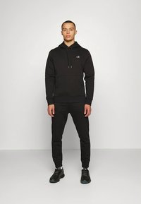 Conjunto de hoodie e calças de treino pretas feitas de mistura de algodão, com detalhe de logótipo no peito, punhos canelados e bolso canguru.