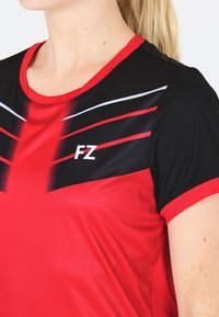 Punainen ja musta urheilupaito, jossa on lyhyet hihat, pyöreä kaula-aukko ja dynaaminen raidallinen kuosi. "FZ" logo valkoisena edessä.