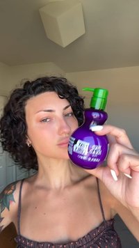 Paarse fles haarproduct met een groene pomp en een gebogen ontwerp en glanzende afwerking. Bevat witte tekst op het etiket.