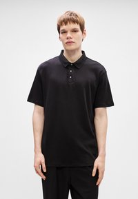 Camisa polo preta de mangas curtas, com colarinho clássico e placket de três botões. Feita de um tecido suave, possui um corte descontraído e sem padrões visíveis.