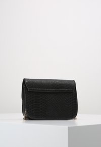 Czarna torebka na ramię z eko skóry o fakturze imitującej wężową skórę. Posiada klapę zamykaną i srebrny łańcuchowy pasek. Kompaktowy, prostokątny kształt.