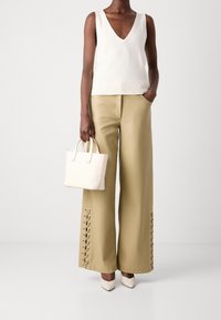 Top senza maniche con scollatura a V color crema, pantaloni larghi beige con dettaglio laccato laterale, borsa bianca e décolleté beige a punta. Texture morbide in tutto il look.