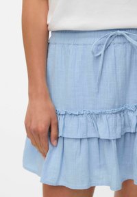 Jupe frisée bleu clair en tissu texturé. Présente une taille élastique avec un cordon de serrage. Possède un ourlet à volants en couches.