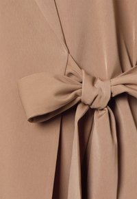 Tissu beige à la texture lisse et à la légère brillance, présentant un nœud attaché au centre et des plis fluides autour de la taille.