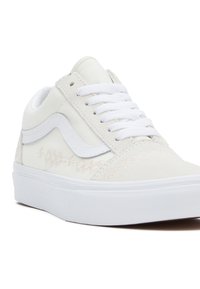 Białe sneakersy z zamszowej cholewki o fakturze, z białymi sznurówkami, paskiem po bokach i subtelnymi haftowanymi detalami. Płaska biała guma podeszwy.