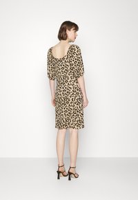 Vestido de padrão de leopardo com costas quadradas, mangas curtas e volumosas, e um corte até ao joelho. Usado com saltos pretos com tiras.