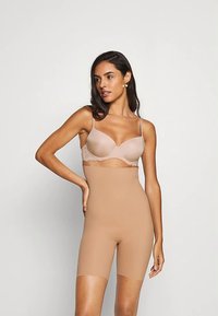 Beige naadloze bodysuit met een aansluitend ontwerp, voorzien van corrigerende shorts en een beha gedeelte met kantaccenten. Zachte stoftextuur.