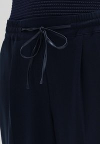 Gros plan sur un pantalon bleu marine foncé avec une ceinture élastique et un cordon fin en tissu noué en nœud à l'avant.