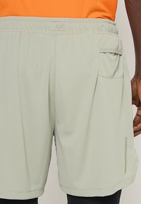 Pantalones cortos deportivos de malla color verde claro con una cinturilla elástica, que incluyen un bolsillo lateral y un pequeño logo cerca del dobladillo.