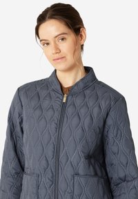 Pikowana granatowa kurtka z kołnierzem stojącym, zamkiem błyskawicznym z przodu, dwiema kieszeniami i teksturą w romby. Miękki, lekki materiał.