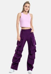 Kitsas roosa crop top, millele on sobitatud tingitud laiad lilla cargo püksid, millel on mitmed suured taskud ja kihilised kangadetailid. Valged tossud.