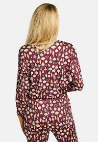 Komplet pižame z dolgimi rokavi v bordo barvi z igrivim prazničnim vzorcem, ki vključuje okraske, drevesa in labode. Mehka, raztegljiva tkanina z udobnim krojem.