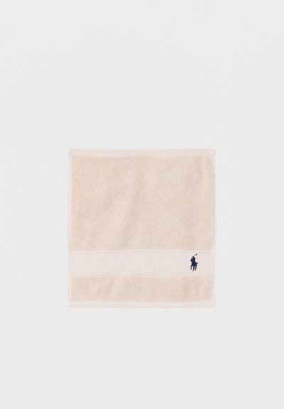 Μπεζ τετράγωνη πετσέτα με υφασμάτινη υφή και ένα μικρό, κεντημένο λογότυπο παίκτη πόλο σε ναυτικό μπλε κοντά σε μία γωνία.