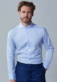 Lichtblauwe button-up shirt met lange mouwen, een spitse kraag en een gladde stof. Draagt zakelijke donkere broek met een getailleerde pasvorm.