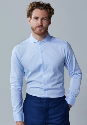 Lichtblauwe button-up shirt met lange mouwen, een spitse kraag en een gladde stof. Draagt zakelijke donkere broek met een getailleerde pasvorm.