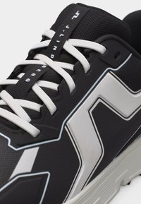 Αθλητικό παπούτσι ασπρόμαυρο με λευκά κορδόνια, μαύρη πλέξη στη γλώσσα και έντονο λευκό γεωμετρικό σχέδιο στην πλευρά.