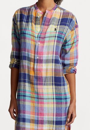 Femme portant une robe-chemise à manches longues à carreaux multicolores avec un col mandarin et un devant boutonné, manches retroussées jusqu'aux coudes.
