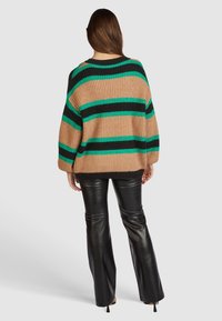 Pull en maille épaisse avec des rayures horizontales beige, noir et vert, doté d'une coupe décontractée et de épaules tombantes. Associé à un pantalon en cuir noir.