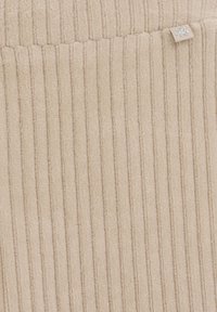 Beige ribbed fabric with a soft texture; features vertical lines and a decorative tag with a snowflake accent.