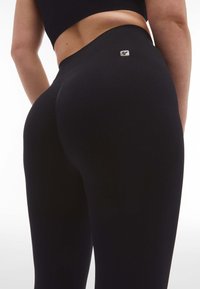 Leggings neri a vita alta realizzati in tessuto elasticizzato, con una texture liscia e un piccolo etichetta logo sulla vita posteriore.