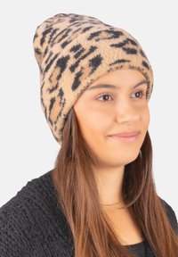 Knit beanie in tan with black leopard print, featuring a soft texture and slouchy design, worn casually.