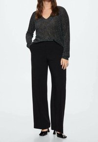 Pantaloni neri a gamba larga con una texture liscia abbinati a un top lungo a maniche con paillettes scuro e scollatura a V.