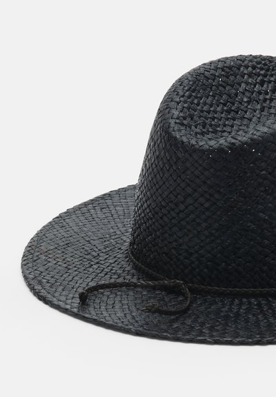 Chapeau noir tissé à large bord avec un ruban tressé noué en boucle, présenté sur un fond clair uni.