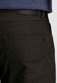 Primo piano di una tasca di jeans in denim marrone scuro con cuciture visibili e un piccolo etichetta nera con la lettera "P".
