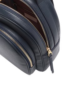 Námořnický kožený batoh se třemi zipovými přihrádky, zdobený zlatými zipy a texturovaným povrchem. Uvnitř podšitý bordó látkou.