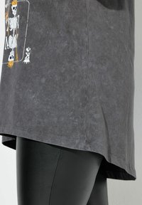 Camiseta de color gris oscuro hecha de una tela suave, con un gráfico de esqueleto en blanco y naranja. Dobladillo curvado, combinada con leggings negros.