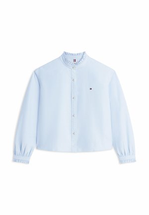 Blouse bleu clair à manches longues avec col et poignets à volants, fermeture à boutons sur le devant, et petit logo brodé sur le côté gauche de la poitrine.