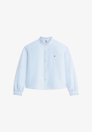 Blouse bleu clair à manches longues avec col et poignets à volants, fermeture à boutons sur le devant, et petit logo brodé sur le côté gauche de la poitrine.