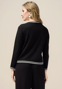Maglione nero con rifiniture bianche al colletto e alle maniche. Presenta un design semplice e aderente con maniche lunghe e orlo dritto.
