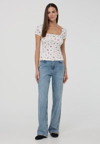 Top bianco a maniche corte con motivo floreale rosa, scollatura quadrata, abbinato a jeans svasati azzurri chiari. Design semplice, vestibilità casual.