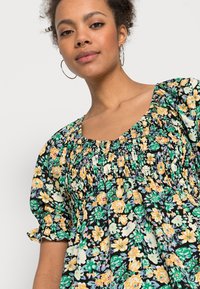 Blusa preta floral com mangas bufantes, apresenta um corpete franzido, flores coloridas em amarelo, verde e roxo, e punhos com elástico e babados.