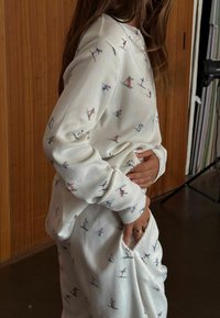 Weißer, gerippter Pullover mit mehrfarbigen kleinen Mustern von Menschen in verschiedenen Posen. Mit langen Ärmeln und Seitentaschen.