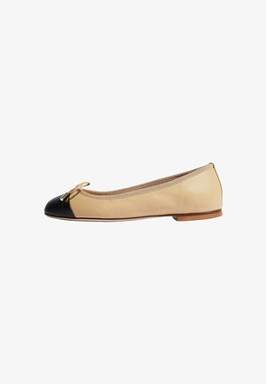 Bailarina de cuero beige con puntera negra, acento de lazo dorado y borde texturizado alrededor de la abertura. Suela plana para un caminar fácil.