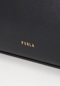 Crna kožna torba s teksturiranom površinom i zlatnim "FURLA" logom. Dizajn je elegantan s minimalističkim naglascima.