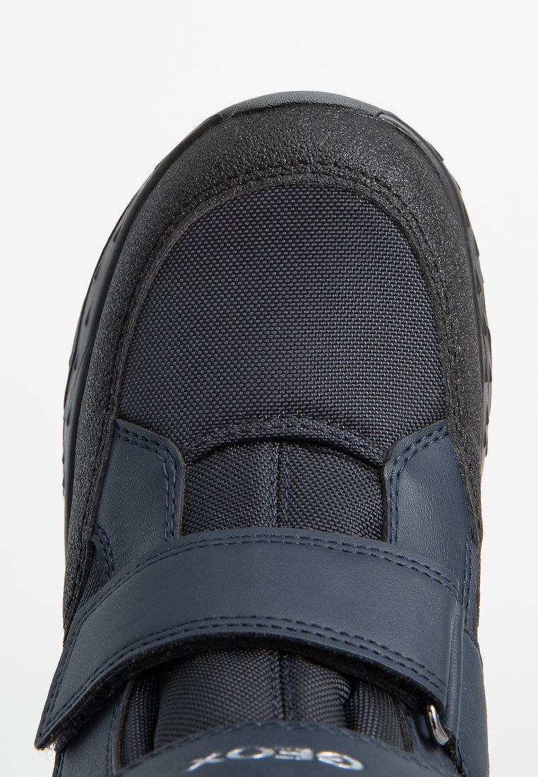 Marineblaue Schuhe mit einem strukturierten, synthetischen Obermaterial und glatten Lederelementen. Sie verfügen über einen breiten Klettverschluss und eine robuste Gummisohle.