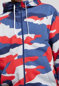 Nike zip-up hoodie i marinblått, rött och vitt kamouflagemönster; har en huva, snören och framfickor med kontrasterande sömmar.