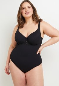 Maillot de bain une pièce noir avec une finition texturée, présentant un décolleté plongeant, un soutien-gorge avec armatures, des bretelles larges, et un anneau doré accentuant le centre.