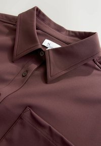 Maroon button-up shirt with a structured collar, smooth texture, two-button closure, and a front pocket. Tag visible inside collar.