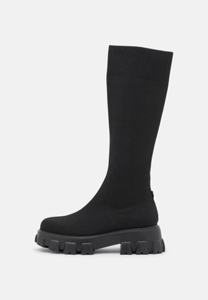Μαύρες πλεκτές μπότες μέχρι το γόνατο με χοντρή καουτσούκ σόλα που διαθέτει υφή και ραβδωτό κολάρο για επιπλέον άνεση και εφαρμογή.
