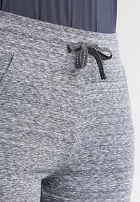 Šedé sportovní kalhoty vyrobené z texturované látky, s bočními kapsami a černou šňůrkou v pase.