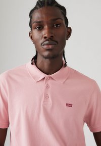 Polo shirt rose clair en coton, avec un col classique, quatre boutons et un petit logo rouge Levi's sur la poitrine.