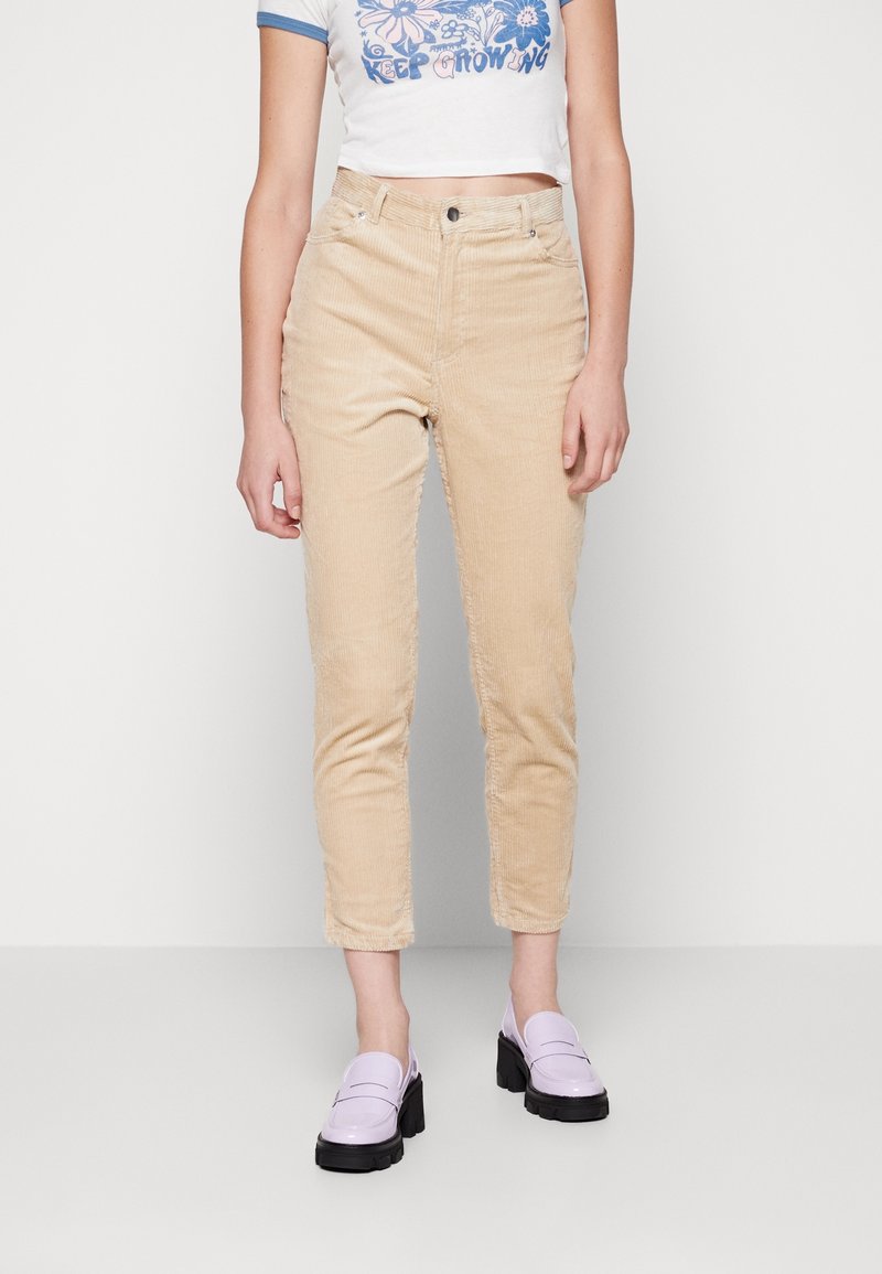 Pantalon en velours côtelé beige à coupe droite et texture côtelée ; porté avec un t-shirt blanc graphique court et des mocassins lavande à semelle épaisse.