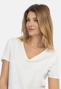 Hvid v-hals t-shirt lavet af letvægtsstof, med korte ærmer, en subtil tekstur og et rent, enkelt design.