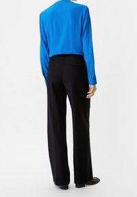 Blusa blu a maniche lunghe abbinata a pantaloni neri su misura, con taglio dritto. Tessuto liscio, polsini con bottoni e design semplice.