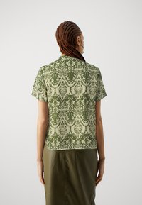 Camicetta a maniche corte di colore verde con un motivo decorativo, caratterizzata da un colletto e una vestibilità comoda, realizzata in tessuto leggero.